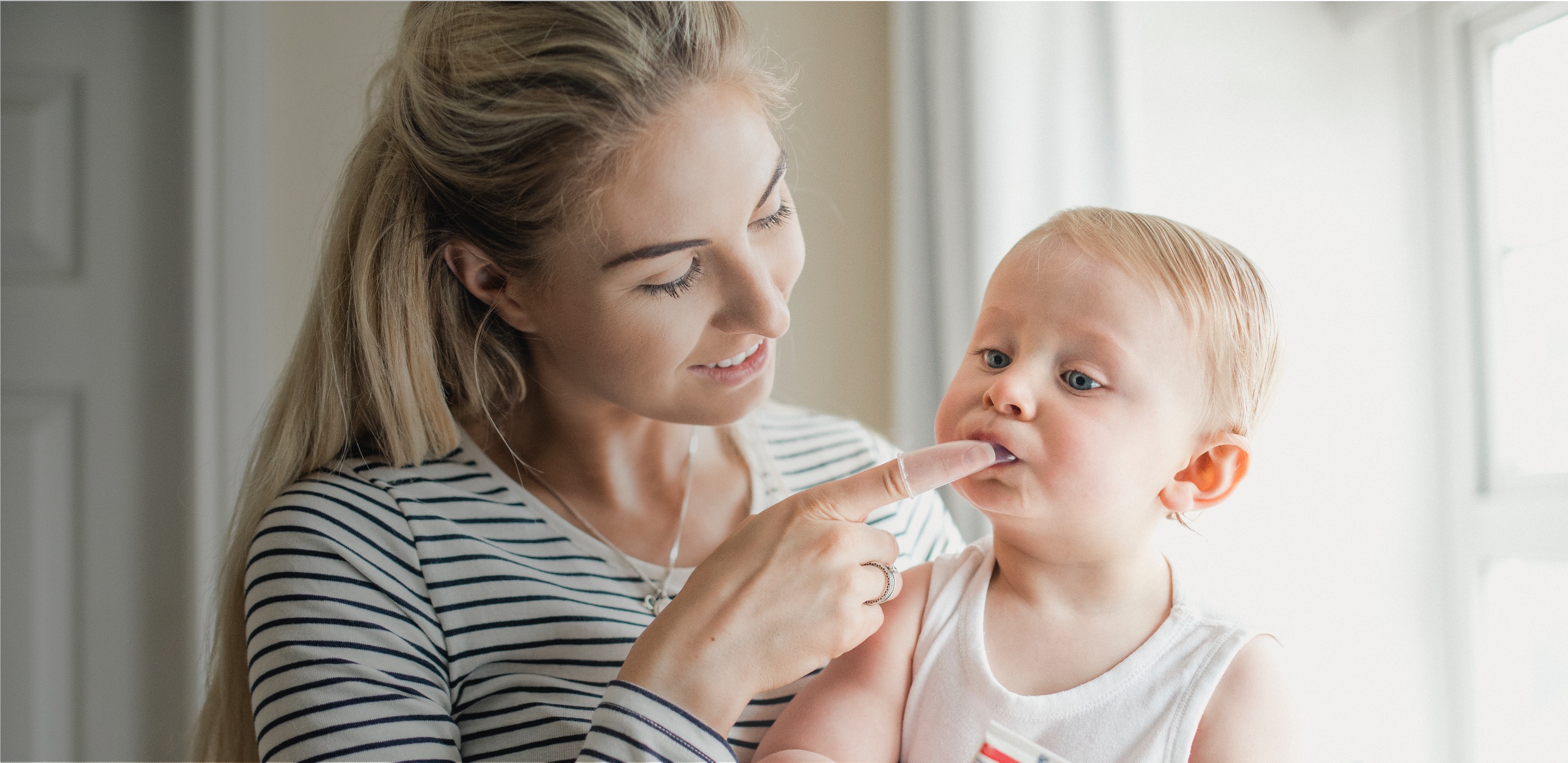 Glückliche Mutter putzt mit der Dentinox Fingerhut-Zahnbürste die ersten Zähnchen ihres Babys